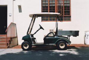 An empty rundown golf cart parked outside an architectural building highlighting the importance of how to change a tire on a golf cart.