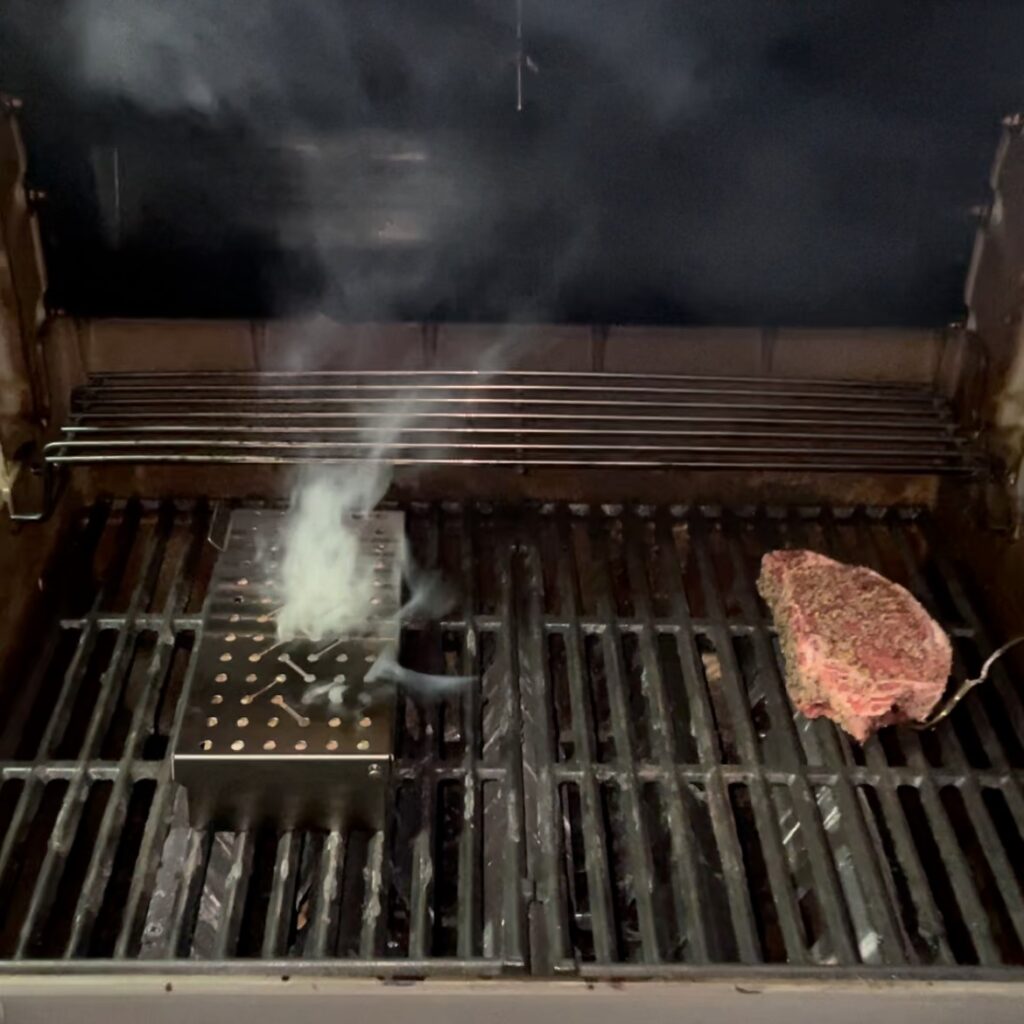 A tantalizing reverse sear steak on the grill with the Weber Smoker Box emitting a rich, smoky aroma.