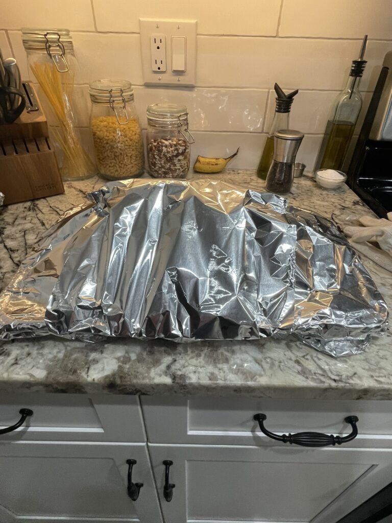 A pork butt tented with tinfoil while resting after being cooked on a Traeger grill.