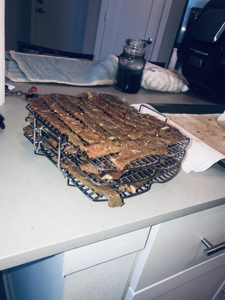 Spicy beef jerky placed on a rack, prepared for dehydration as part of the Ninja Foodie Grill recipe.