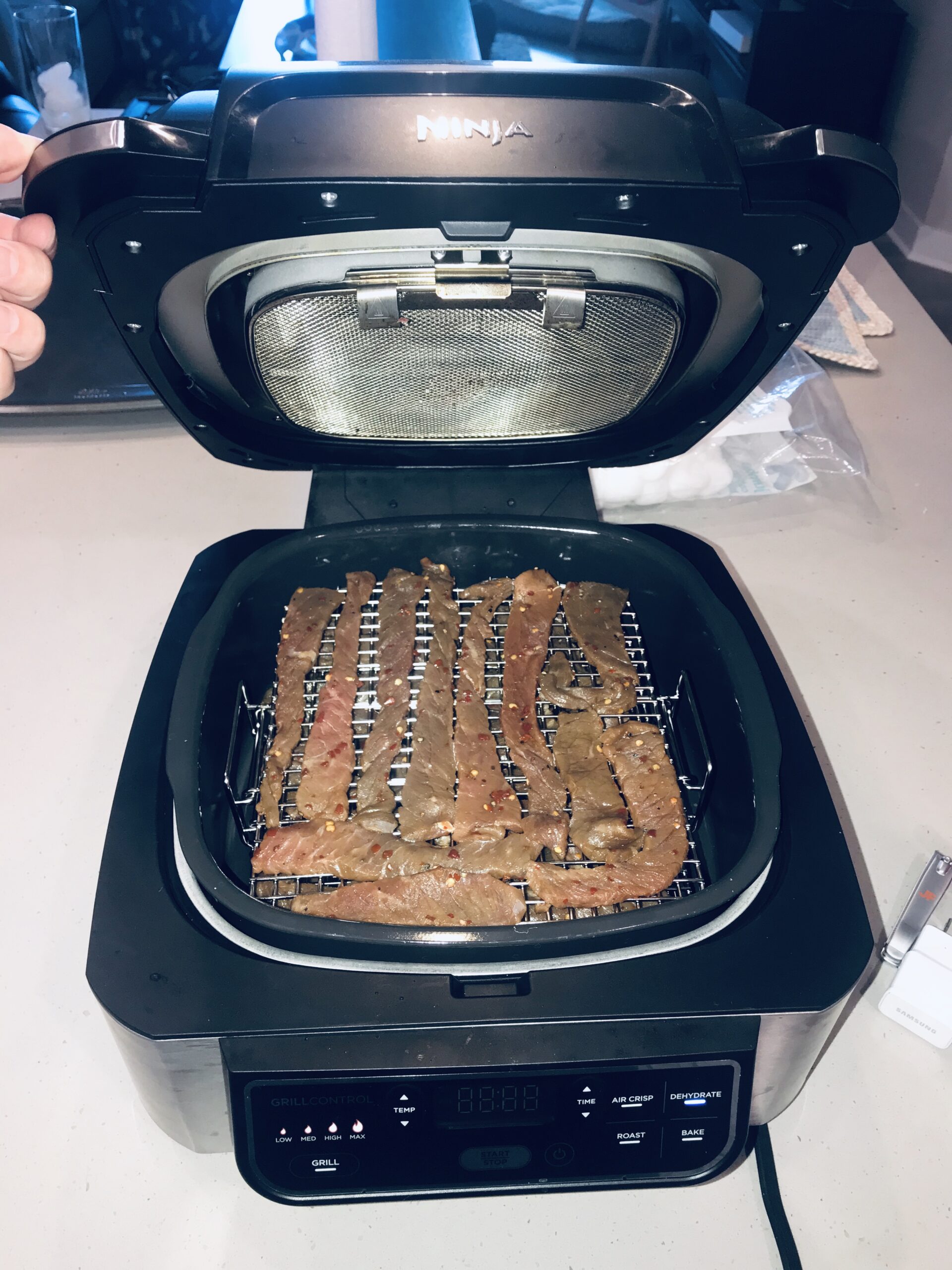 Spicy beef jerky placed in the Ninja Foodi Grill, set to dehydrate.