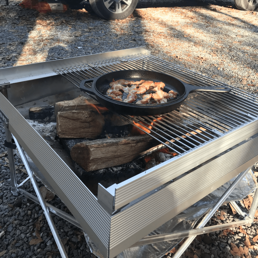 Fresh bacon sizzling on portable grates over a pop-up fire pit, demonstrating the versatility of a fire starter for camping