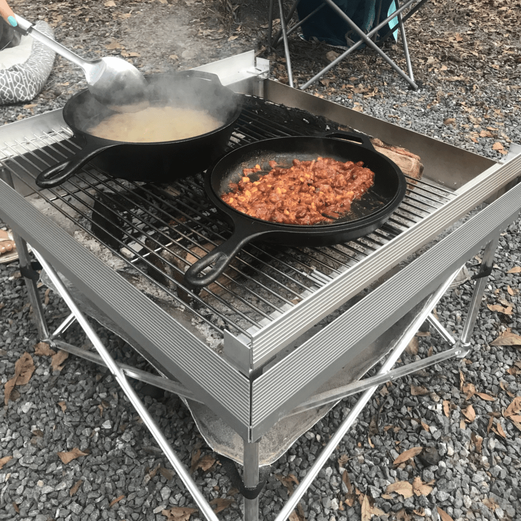 A hearty chili dish being prepared in two cast iron pieces over a campfire grill, showcasing the practical applications of a camping fire starter.