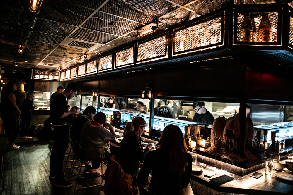 A bustling scene inside Double Knot, a renowned Japanese restaurant Philadelphia based, showcasing chefs expertly grilling food using the Robatayaki method.