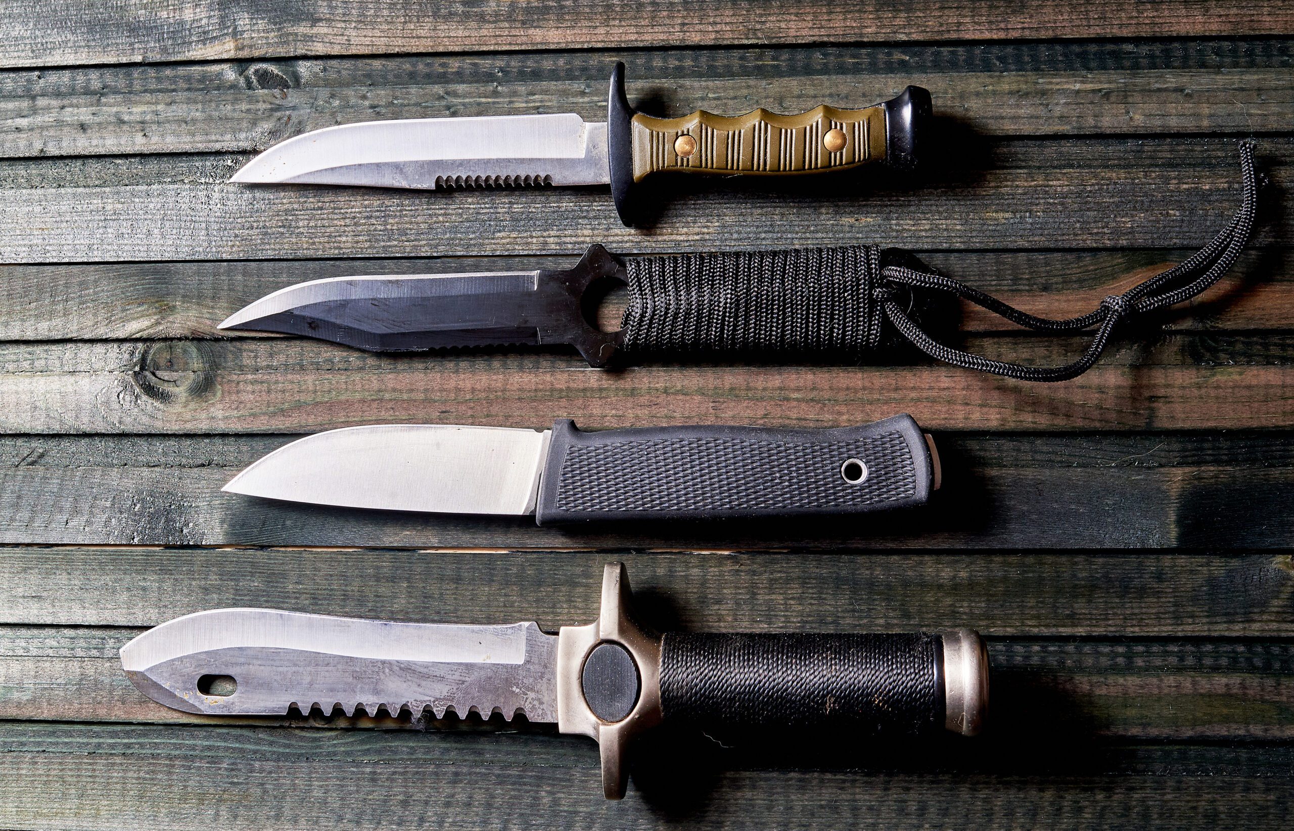 Multiple survival knives with different fixed blades laid out on a rustic wooden surface.