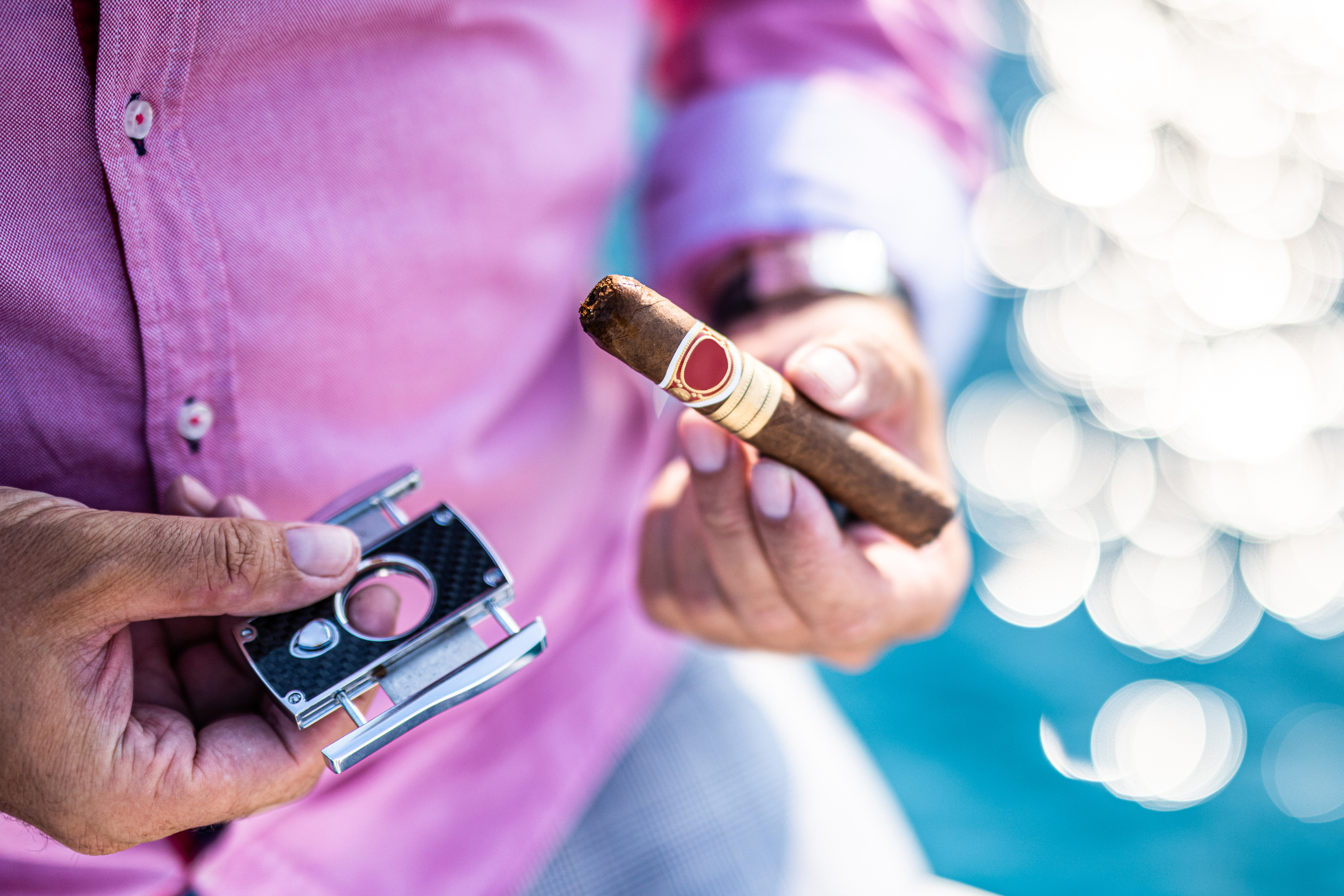 A man is seen holding a cigar and a cigar cutter, preparing to demonstrate how to cut a cigar.