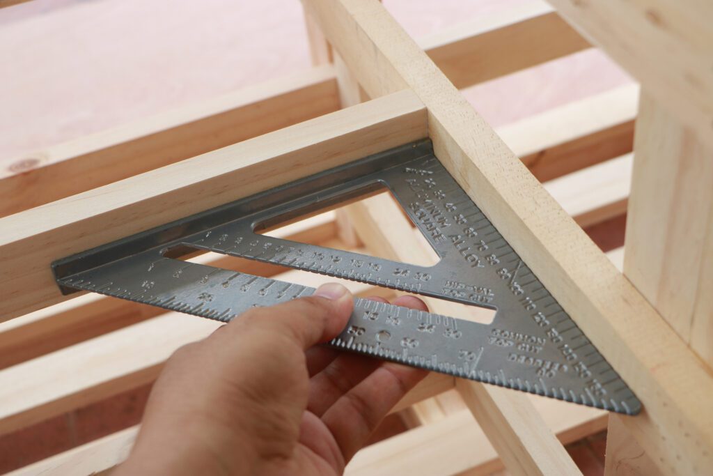 Carpenter measuring an angle on a piece of wood using a speed square.