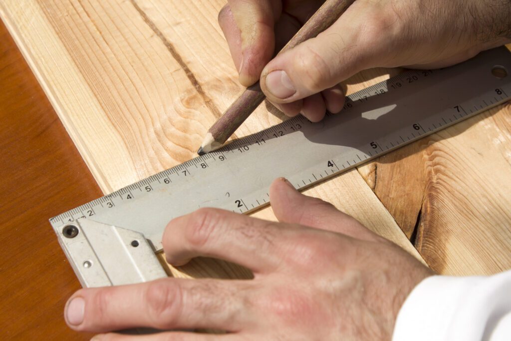 Man using a large framing square to measure and mark a wooden board.