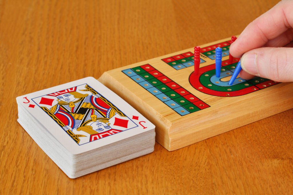 Crib board and deck of cards during a cribbage game, showing players progressing with their pegs and the concept of 'the crib' in cribbage