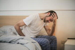 Man sitting on bed clutching his lower back in pain, illustrating the impact of the worst sleeping positions for lower back pain.