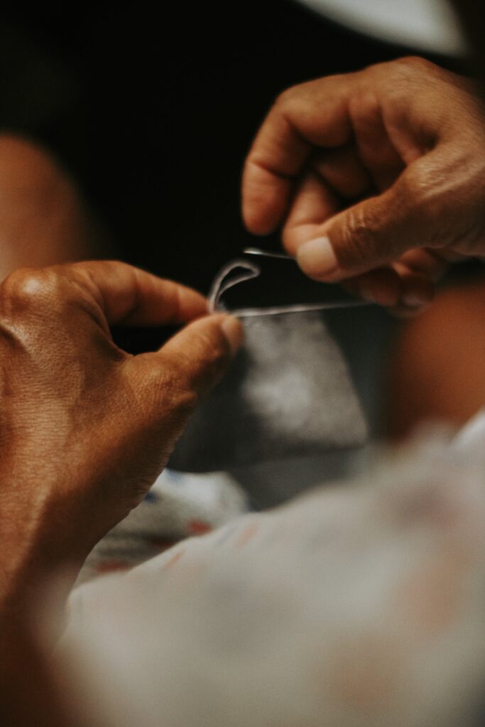 Close-up of hands deftly holding a needle and thread, demonstrating the initial steps on how to sew a hole in fabric.