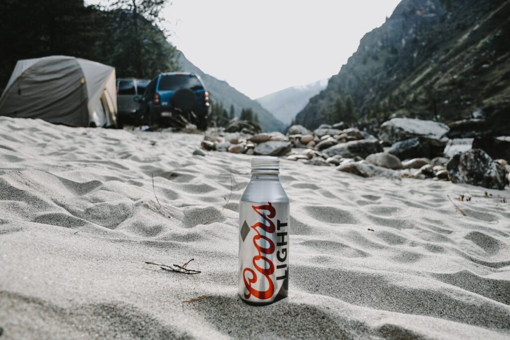 Can of Coors Light showcasing its low calories and eliminating the question "how many carbs in coors light". It is placed on a sandy beach under the clear blue sky, illustrating the beer's appeal to health-conscious consumers.