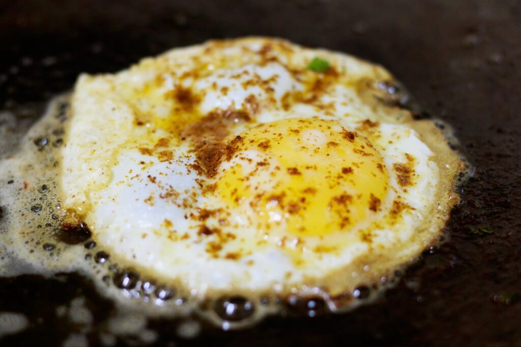 Close-up view of an over hard egg being prepared in a frying pan, demonstrating how to make over hard eggs.