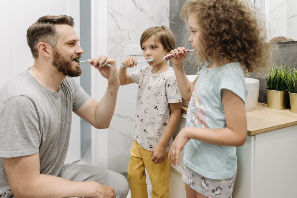 A man teaching his kids the importance of brushing teeth and incorporating the best mouthwash for overall gum health.