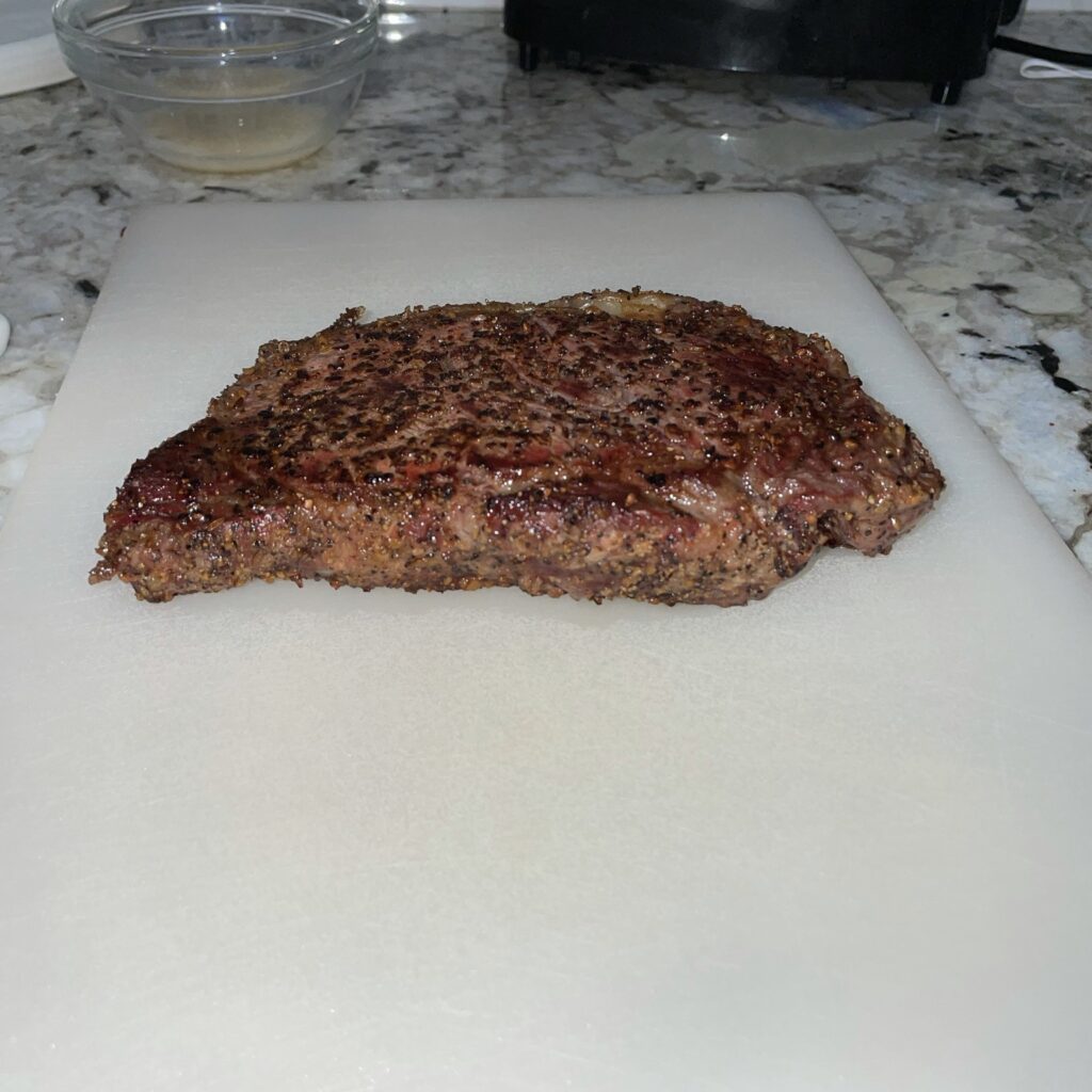 A perfectly cooked reverse seared ribeye steak is resting after grilling, allowing the juices to redistribute.